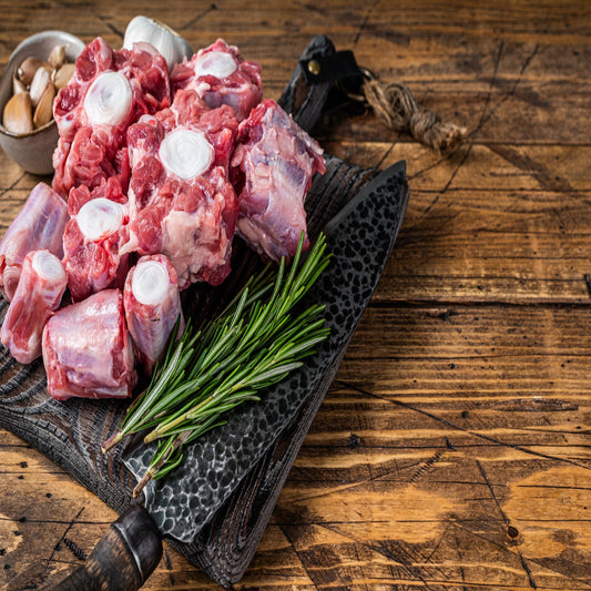 Raw ox tail meat displayed on a wooden cutting board with a sprig of rosemary, alongside a knife for cutting.